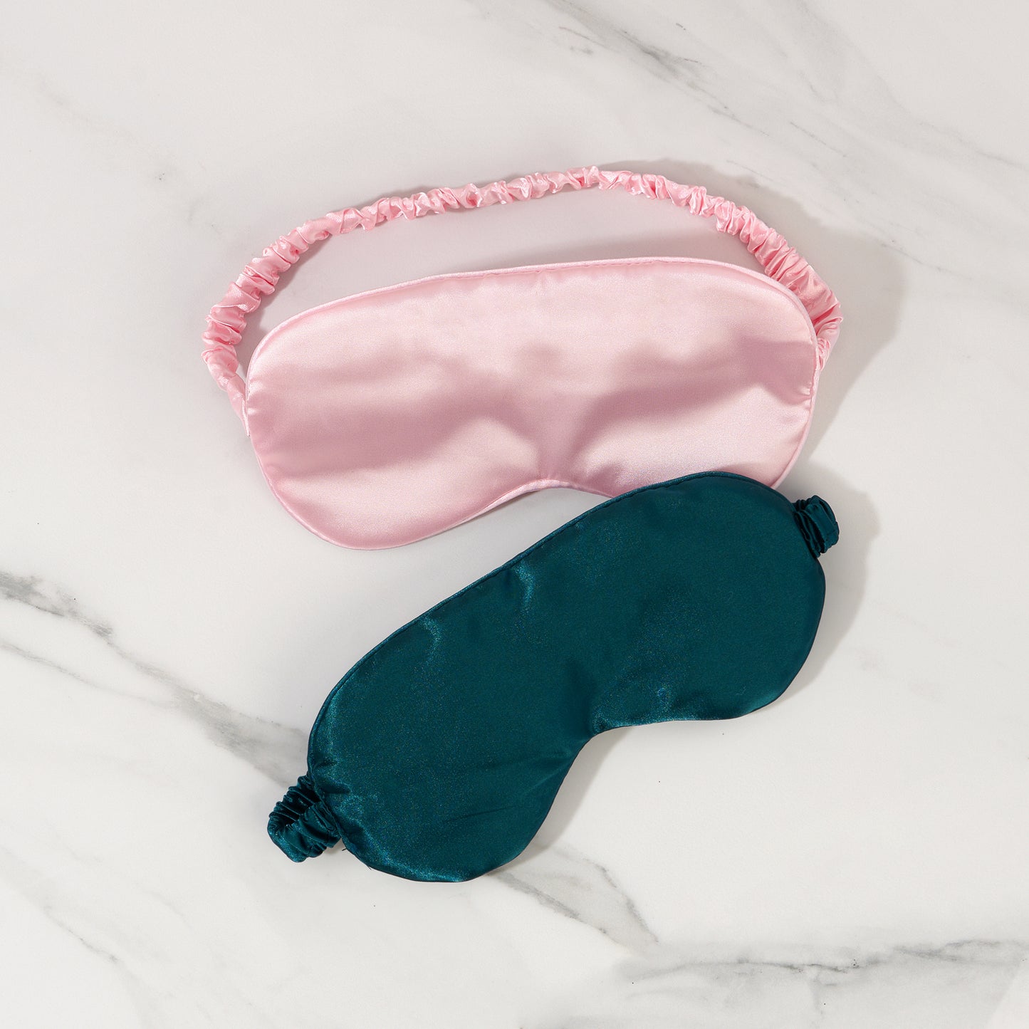 Pink and teal satin eye masks on a marble surface