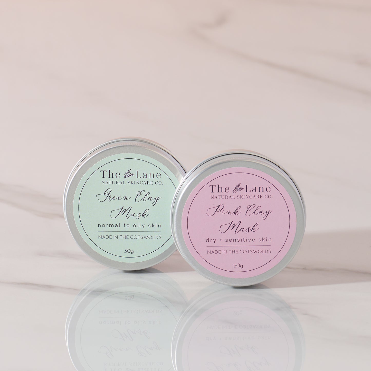 Two tins of The Lane Natural Skincare Co. clay face masks on a light pink background