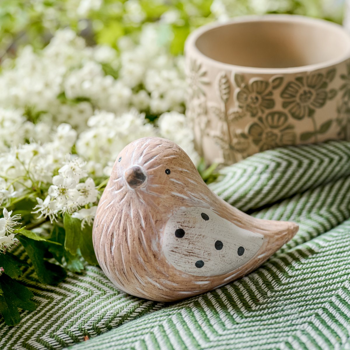 A small terracotta bird ornaments at the front with a floral green and beige planter behind.