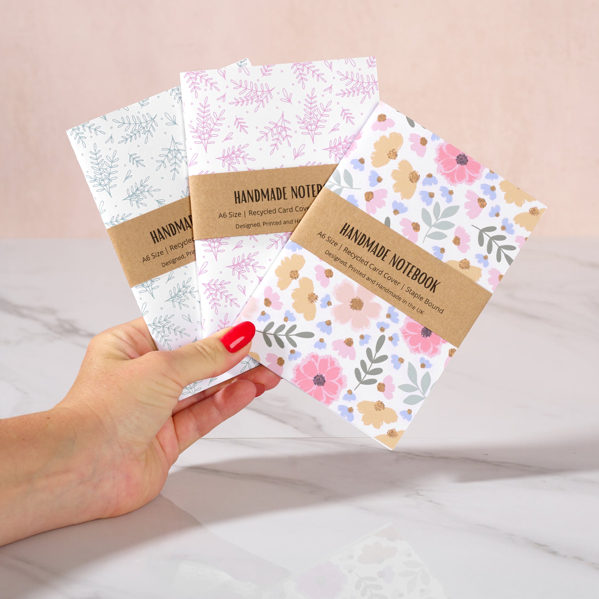 Handmade notebooks with floral designs held by a hand against a light background