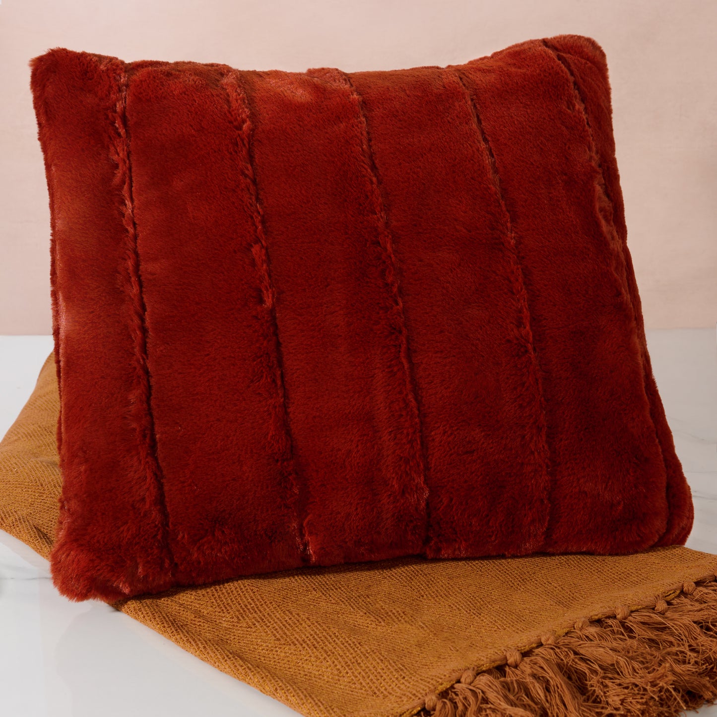 Rust textured pillow on a brown blanket with a beige background