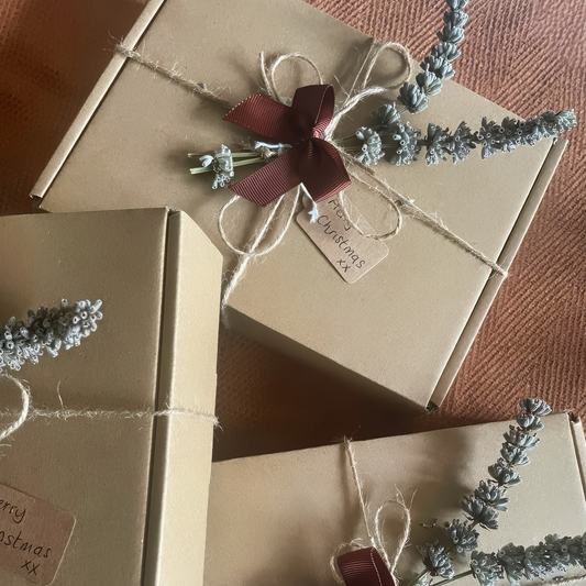 Gift boxes wrapped in brown paper with string, ribbons, and lavender sprigs on a textured surface.