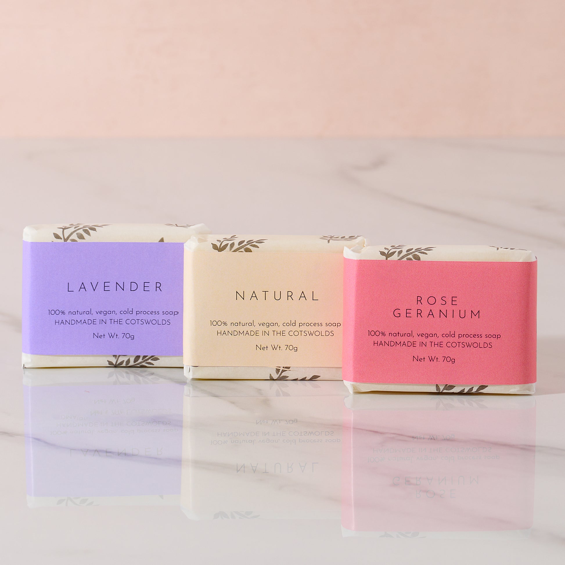 Three bars of soap in different scents with their packaging on a marble surface.