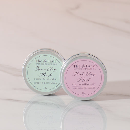 Two tins of The Lane Natural Skincare Co. clay face masks on a light pink background