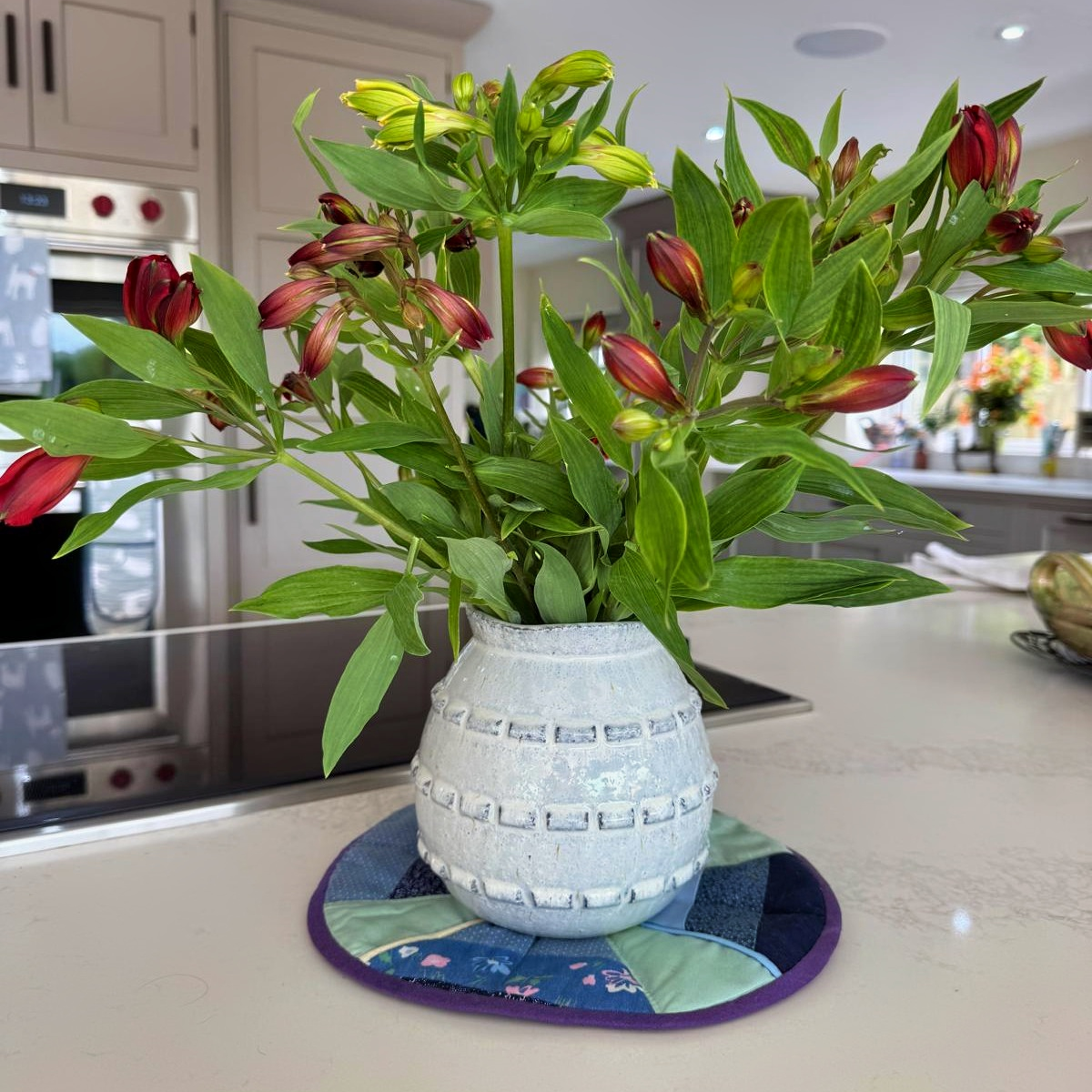 Bouquet of red and green flowers in a textured white vase on a kitchen counter.
